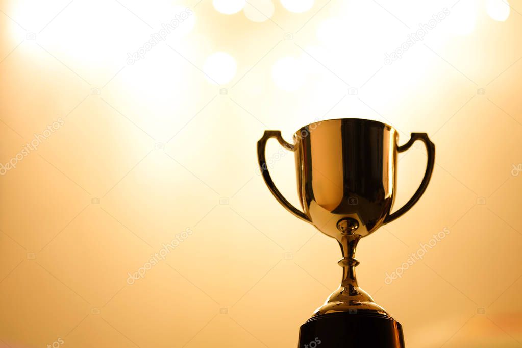 Gold Trophy competition in the dark on the abstract blurred light background with copy space, Spectacular success Concept