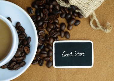 Kahve çekirdekleri, fincan ve iyi başlamak kahverengi zemin üzerine yazılan yazı tahtası Üstten Görünüm.