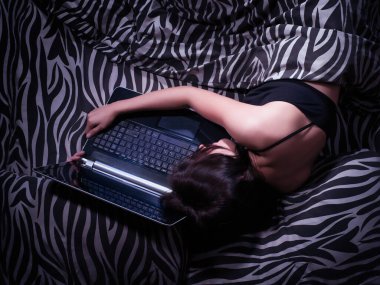 Bilgisayarda yatakta uyuyan bir kadın. Çevrimiçi bağımlılık, sanal hayat ve sanal aşk kavramı. Görünümün üstünde, tonlu resim