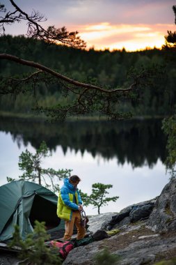 Genç dağcı bir uçurum, gün batımı arka plan pitoresk bir gölde bir üst üzerinde bir kampı olmasının. 
