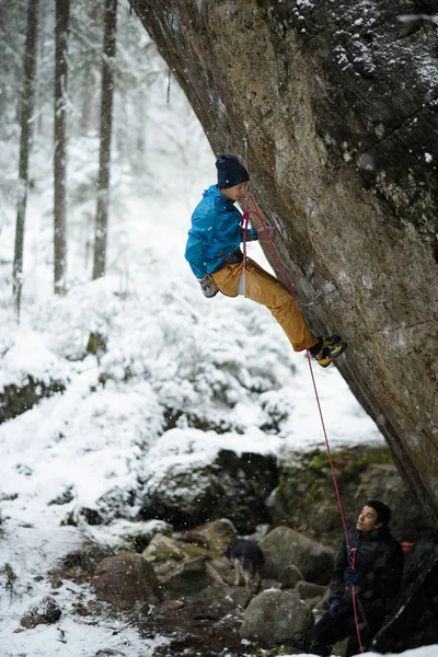 Escalada extrema de deportes de invierno. Joven escalador masculino en una pared de roca. Bosque nevado en el fondo , — Foto de Stock