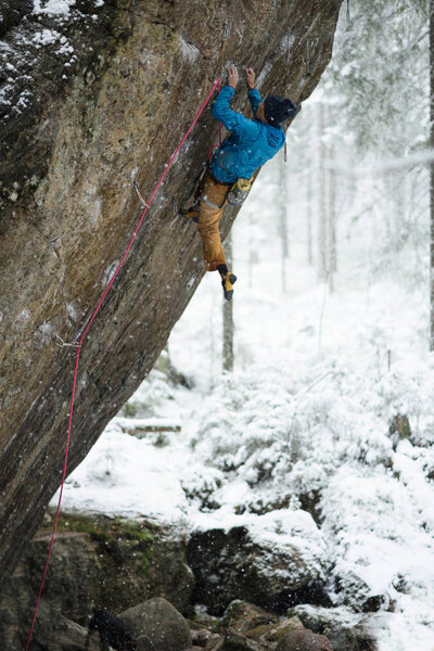 Mountain climber ascending a rock in winter snowy forest. Extrem sports. Karelian nature. 