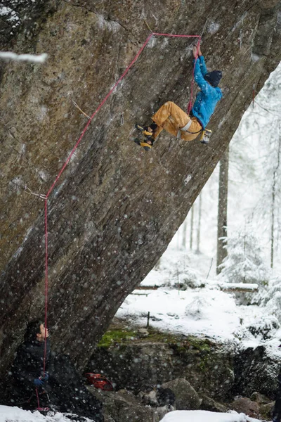 Escalada extrema de deportes de invierno. Joven escalador masculino en una pared de roca. Bosque nevado en el fondo . —  Fotos de Stock