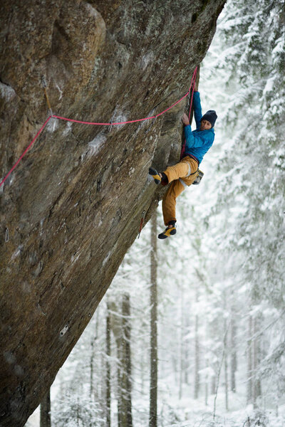 Extreme winter sport. Young man climbing a rock with belay. Rope climbing. 