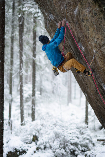 Extreme winter sport. Young man climbing a rock with belay. Rope climbing. 