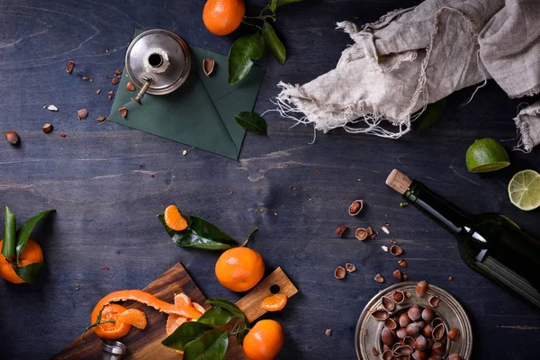 Las mandarinas maduras sabrosas con las hojas con las avellanas y la botella del vino a la mesa. Vista superior, espacio de copia . — Foto de Stock