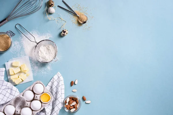 Hälsosam bakning ingredienser - mandel nötter, ägg, smör, mjöl, kex över en blå tabellbakgrund. Bageriet bakgrund ram. Ovanifrån, kopia utrymme. — Stockfoto