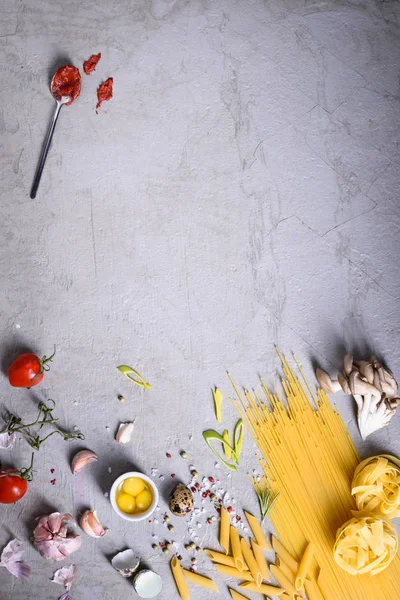 Variété de pâtes avec sauce tomate et oeufs de caille. Ingrédients de la cuisine italienne sur fond gris. Espace de copie, vue du dessus . — Photo