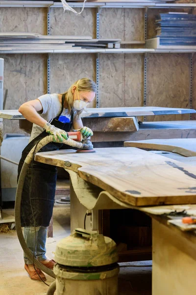 Inside the Wood Industry or Lumber Industry private sector, production of forest products. Female carpenter making slab furniture products, working in a mask and gloves at her workshop.