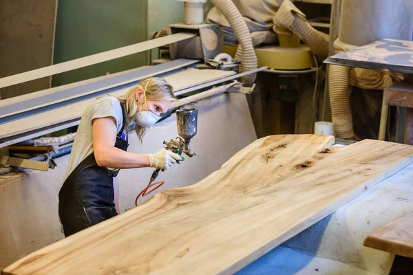 Inside the Wood Industry or Lumber Industry private sector, production of forest products. Female carpenter making slab furniture products, working in a mask and gloves at her workshop.