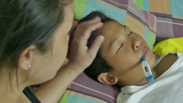 Over the shoulder close up of multicultural Asian mother with sick son lying in bed. — Stock Video