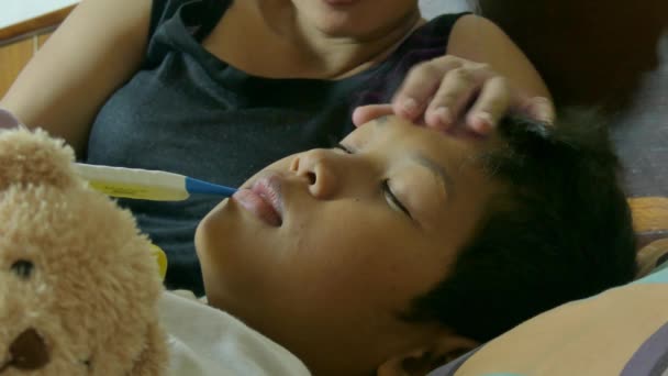 Close up of a multicultural Asian boy sick in bed (profile with mother's thermometer) — Stock Video