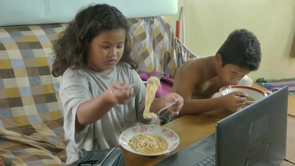 Πολυπολιτισμική Ασίας αδέλφια, παρακολουθείτε ένα βίντεο ενώ τρώνε νουντλς για το μεσημεριανό γεύμα — Αρχείο Βίντεο