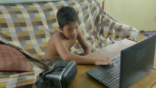 Multicultural Asian boy uses a laptop with a VR virtual reality headset nearby — Stock Video