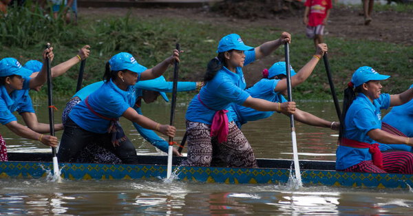 SIEM REAP, CAMBODIA - NOVEMBER 2016: Team of women boat racers with blue jerseys in action as they race towards the finish line during traditional boat races in Cambodia, Southeast Asia