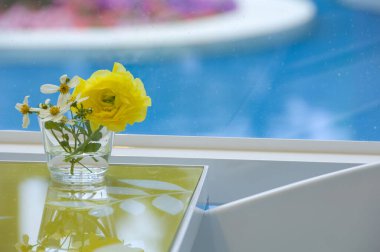 Masanın üzerindeki cam bardakta durgun sarı ve beyaz çiçeğin düzenlenmesi.