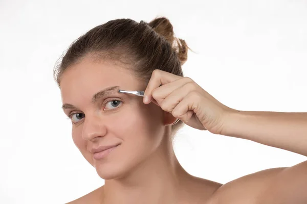 Menina puxa suas sobrancelhas com pinças de metal em um branco — Fotografia de Stock