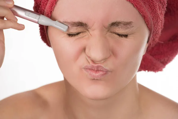Young girl in a red towel caring for your eyebrows with trimmer — Stock Photo, Image