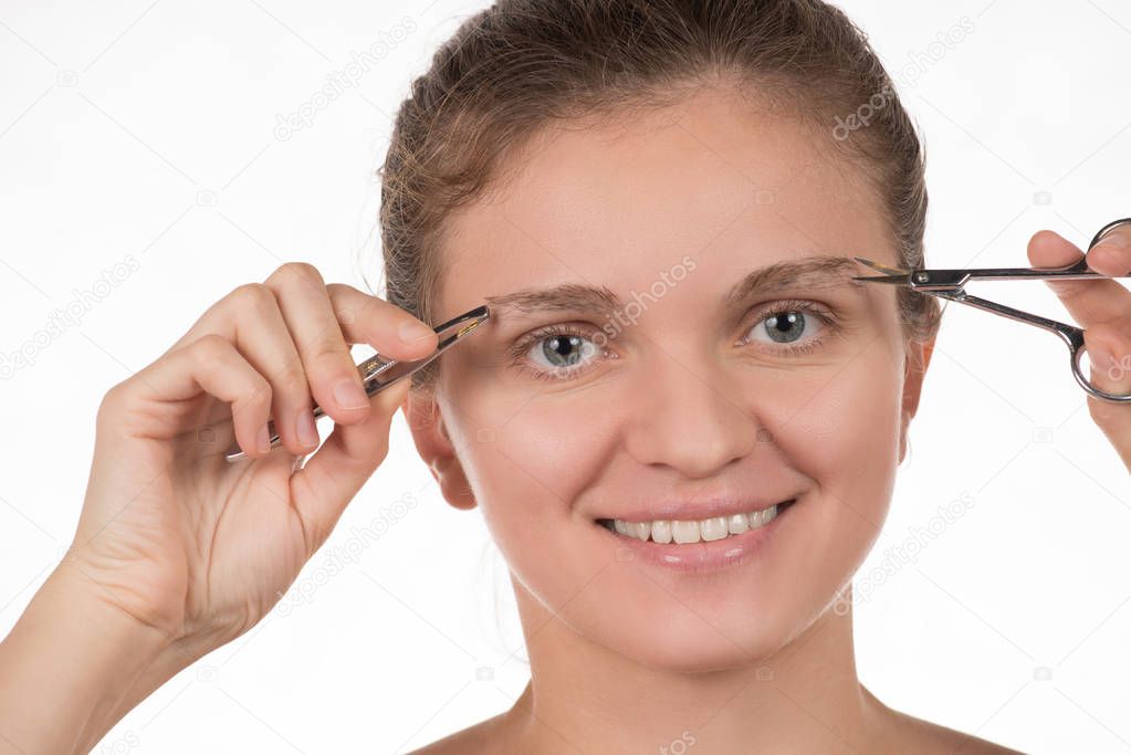 Young girl pulls out her eyebrows with tweezers metal on a white
