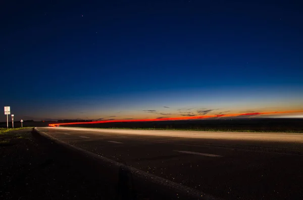 Estrada rural no crepúsculo com os faróis de passar carros nele — Fotografia de Stock