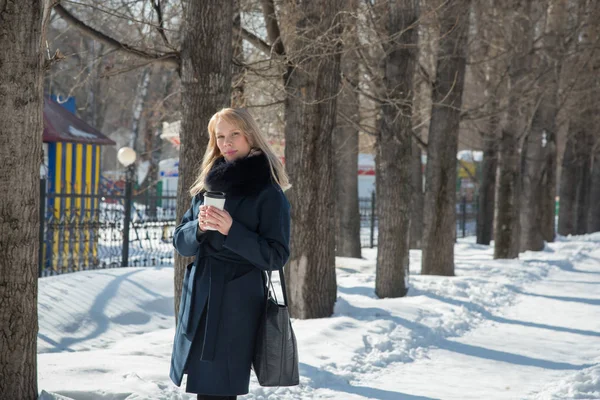 Beautiful girl walking in winter city park with a bag and drink — Stock Photo, Image