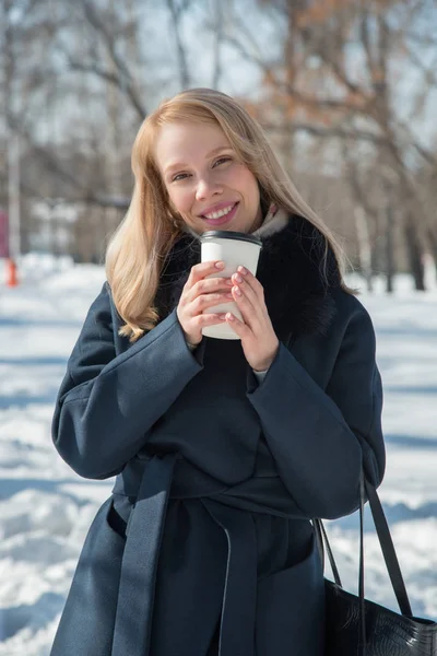 Beautiful girl walking in winter city park with a bag and drink — Stock Photo, Image