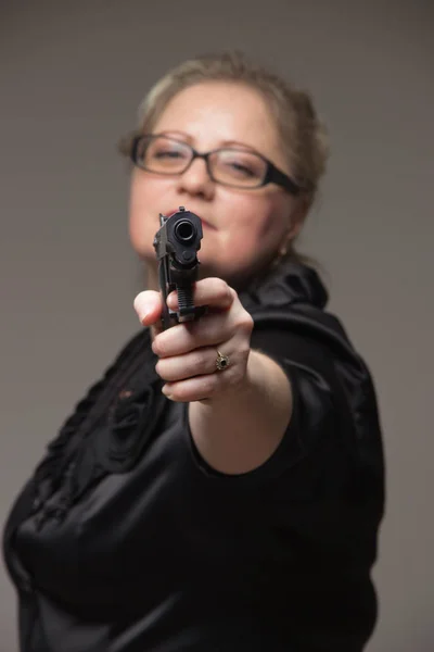 Volwassen zakenvrouw met zwarte pistool op een grijze achtergrond — Stockfoto