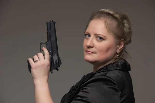 Volwassen zakenvrouw met zwarte pistool op een grijze achtergrond — Stockfoto
