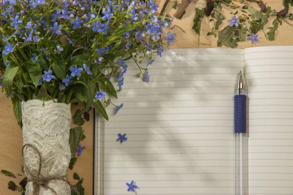 Ein Strauß Blumen vergissmeinnicht, Notizbuch und Stift auf dem hölzernen T — Stockfoto