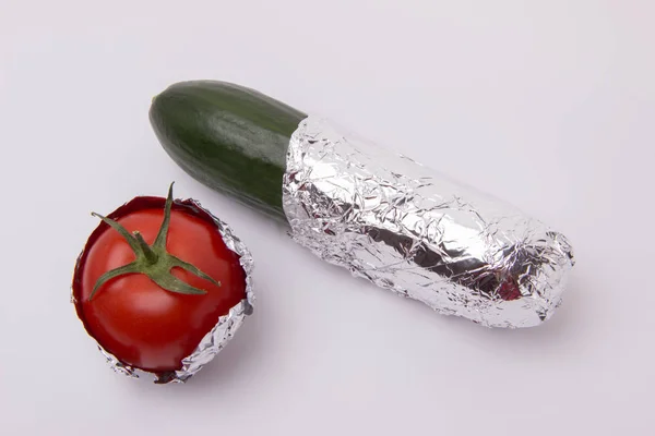 Pepino verde y tomate envueltos en papel de aluminio sobre un fondo blanco — Foto de Stock