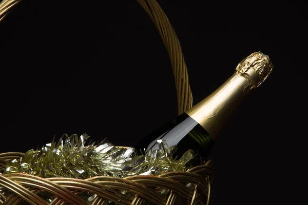 Una bottiglia di champagne in un cesto di paglia con fili di lame di Capodanno a — Foto Stock