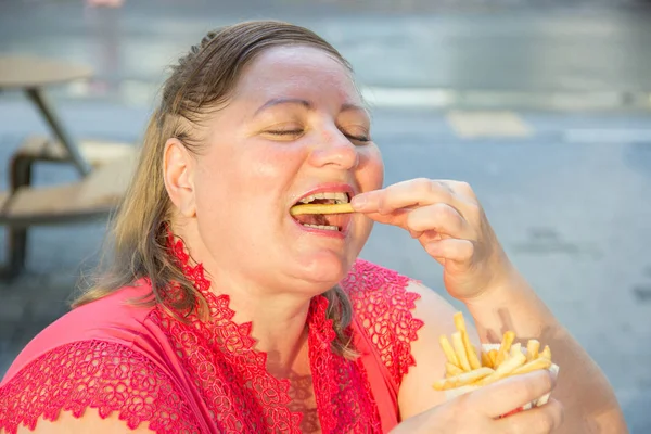 Mujer gruesa comiendo hamburguesa de comida rápida y papas fritas en un café —  Fotos de Stock