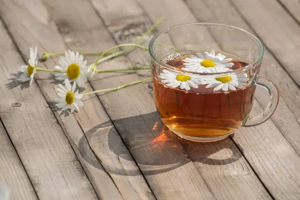 Kräutertee mit Kamille auf einem Holztisch an einem sonnigen Sommertag — Stockfoto