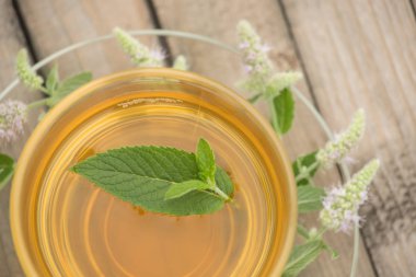 Bir cam kupa ile altın çay yaprakları ve yaz aylarında çiçek standları bir daire ve bir ahşap masa nane