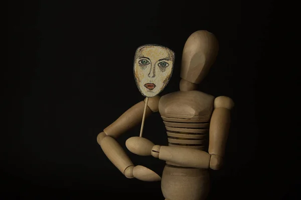 Ξύλινη κούκλα στις αρθρώσεις κατέχει μια μάσκα στα χέρια και να καλύπτει το πρόσωπό της σε μαύρο φόντο — Φωτογραφία Αρχείου