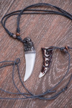 Big bear tooth and bone pendants carved from deer on a brown background clipart