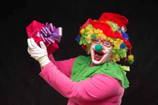 Rolig clown med hår och en glad make-up håller en gåva — Stockfoto