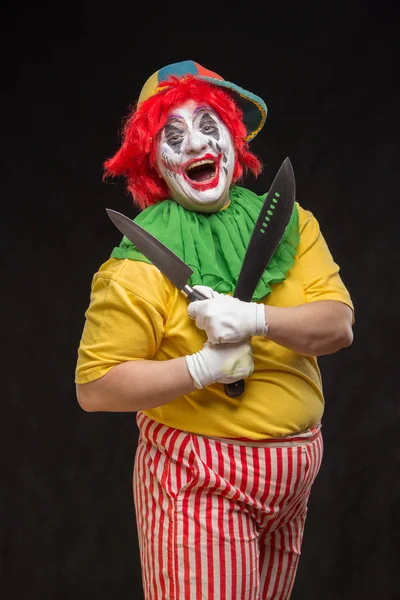 Scary clown with a horrible make-up laughs and with knives in ha — Stock Photo, Image