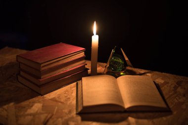 Büyülü bir top, bir parşömen, bir mum ve gecenin karanlığında eski bir kitap.