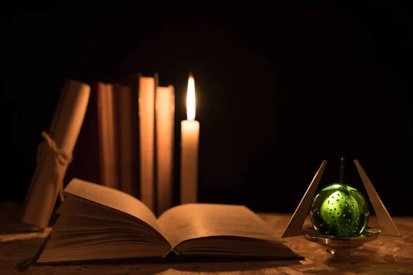 Una bola mágica, un pergamino, una vela y un viejo libro en la oscuridad de la noche —  Fotos de Stock