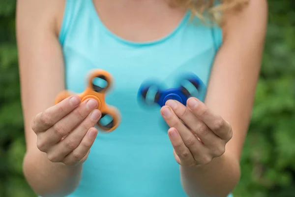 Egy fiatal lány, gazdaság, és csavaró két spinners a kék és orángután — Stock Fotó