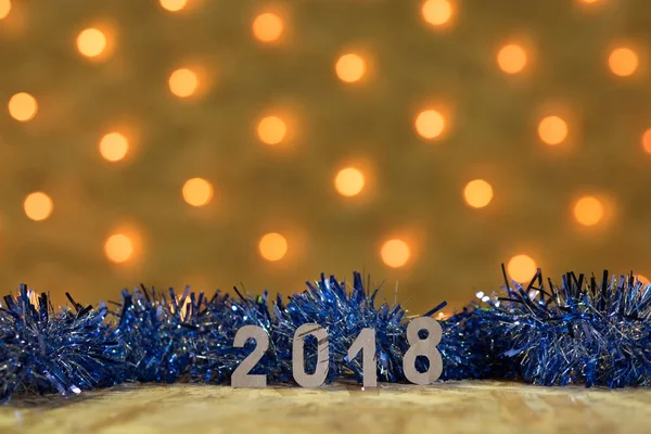 Синя мішура з фігурами 2018 року на столі на фоні новорічної гірлянди з золотими вогнями — стокове фото