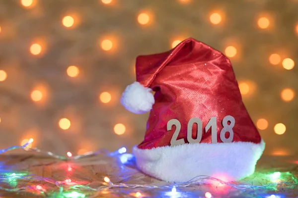 2018 arka planda bir yılbaşı Garland bulanık altın ışıklı bir masaya rakamlar ile kırmızı bere