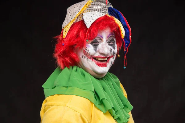 Een afschuwelijk clown met een verschrikkelijke make-up en hoed lachen op een b — Stockfoto