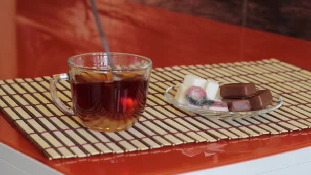 Flickan uppviglar socker med en sked i en mugg med te och en närliggande tefat med socker och sötsaker — Stockvideo