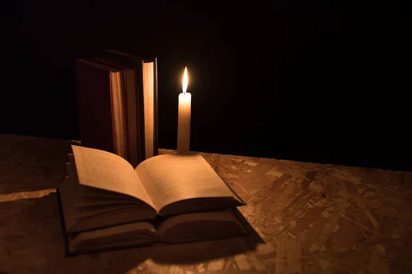 Oude boeken en brandende kaars op een houten tafel op een nacht — Stockfoto