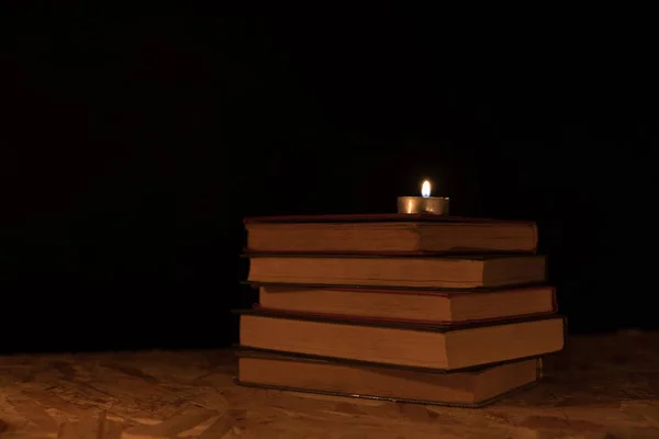 Oude boeken en brandende kaars op een houten tafel op een nacht — Stockfoto