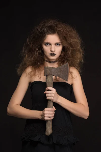 Mooi meisje met een make-up als een heks glimlacht en houdt een bijl op een zwarte achtergrond voor de vakantie van Halloween — Stockfoto