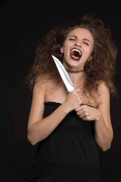 Krásná dívka s make-upem jako čarodějnice usměje a drží nůž na černém pozadí pro svátek Halloween — Stock fotografie
