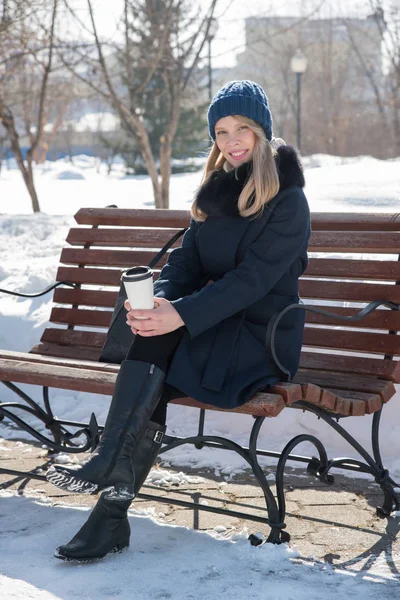 Beautiful young woman on a bench a sunny winter day with a coffe — Stock Photo, Image